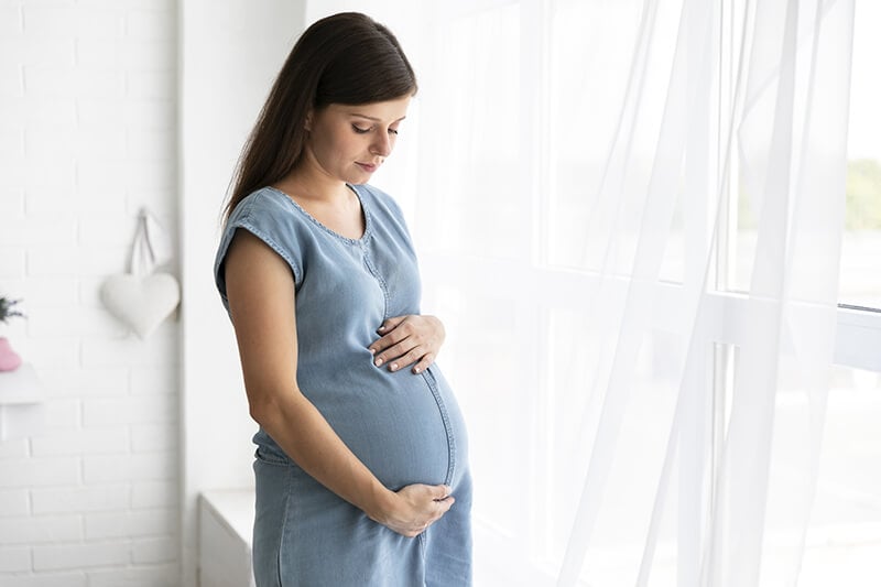 medium shot pregnant woman standing window -